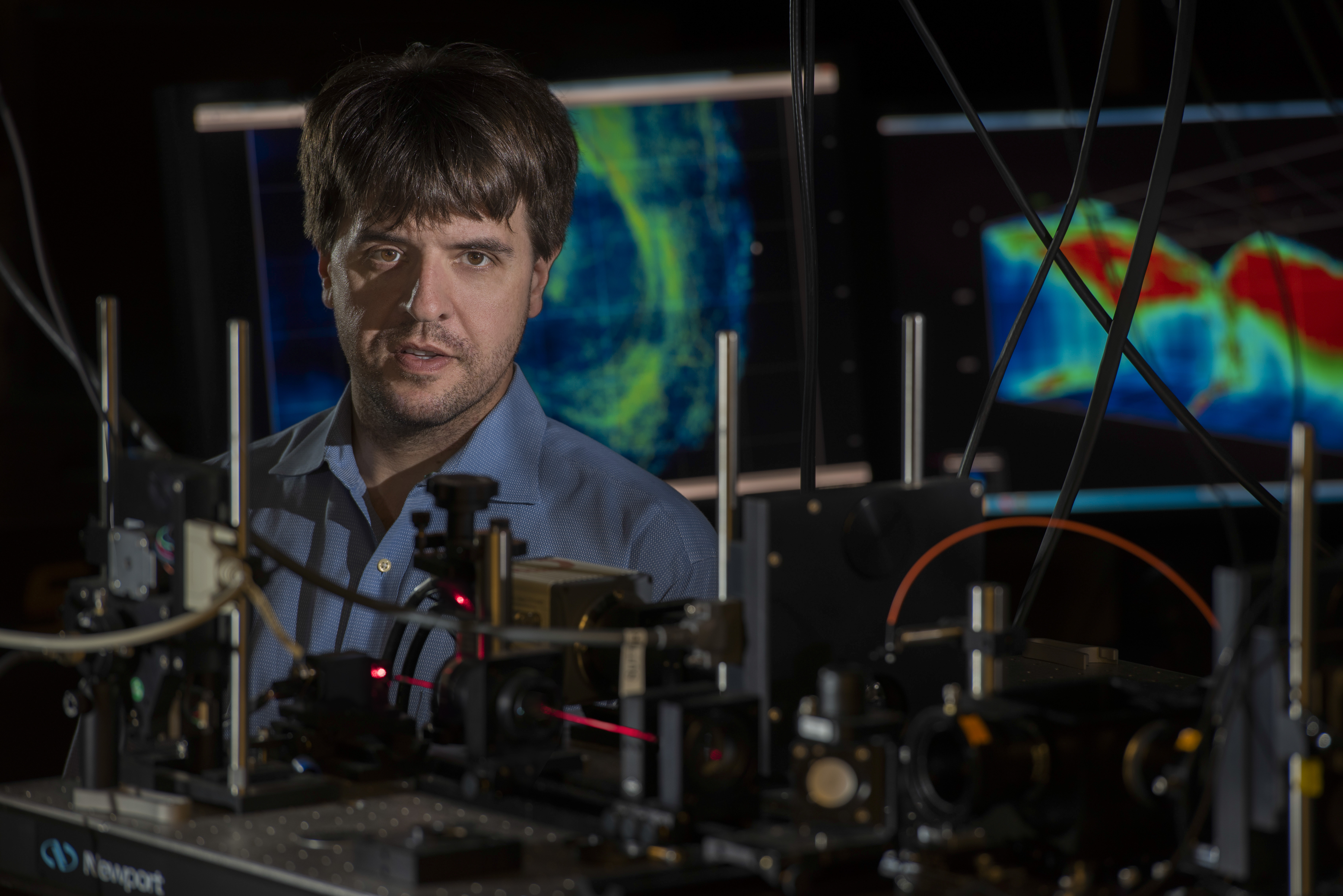 Karl Desseroth in lab behind microscopes with flourscent microscopy images in background 