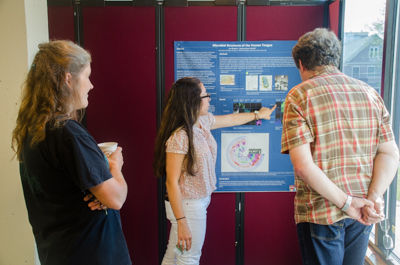 University of Chicago student Isa Alvarez shows her poster to MBL scientist Michael Shribak, right. She studied the human tongue microbiome with MBL Associate Scientist Jessica Mark Welch, at left.