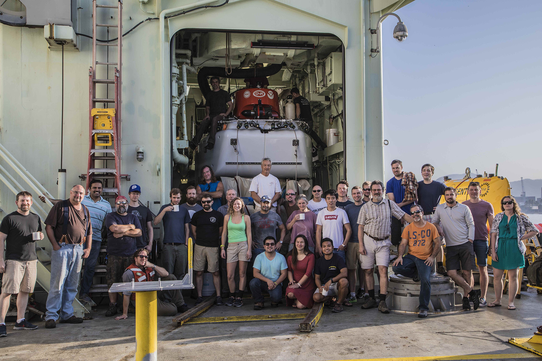Participants in the R/V Atlantis expedition to Guaymas Basin in 2016. The R/V Atlantis is operated by Woods Hole Oceanographic Institution and its expeditions include scientists from many institutions. Deep-sea research is an interdisciplinary team effort that would not be possible without the input of numerous colleagues, crew members, and funding agencies. At rear, the deep-sea submersible Alvin is tucked away in its hangar. Credit: Alexander Epp, Woods Hole Oceanographic Institution
