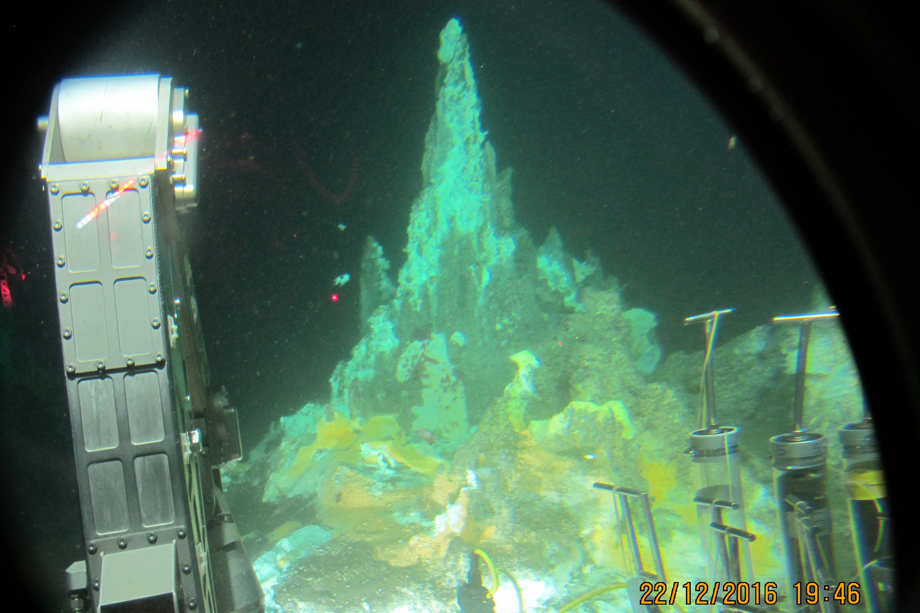 Photo 1: Hydrothermal mound at ~2000 meters depth in the Guaymas Basin. This several meter tall “living” tower of hydrocarbon-soaked minerals and sediments is permeated by hydrothermal fluids. The surface of the structure is covered with white and orange mats of bacteria that use sulfur as an energy source. Seen from the submersible Alvin. Credit: Teske et al, Front. Microb., 2021