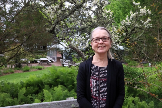 A woman stands outside in front of trees.