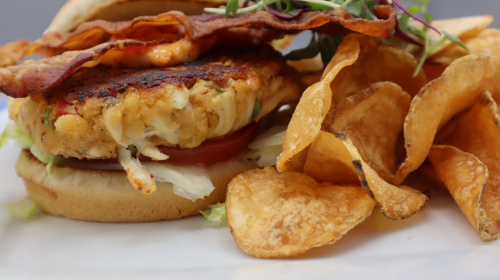 Seafood cake sandwich with bacon and chips.