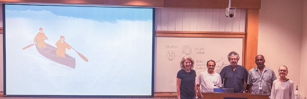 A group of scientists on a stage in front of a documentary screen.