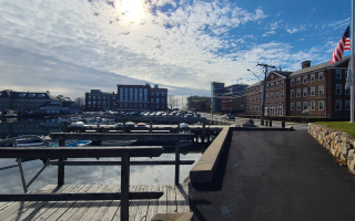 This photo shows an overview of the Marine Biological campus next to the water. The sun is shining above an American flag on the left side of the picture.