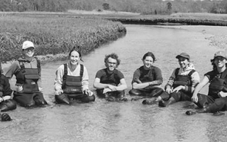 Seven scientists in waders sitting in a salt marsh.