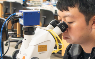This photo shows a student peering into a microscope with the text "Embryology 2026" on top.