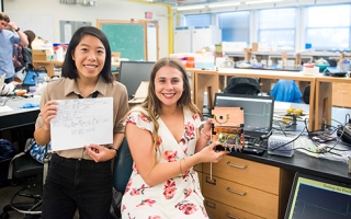 Christina Ford and Alyssa Condie display the plans for and the patch clamp amplifier that they built from scratch in the "Proteins in Action" course. 