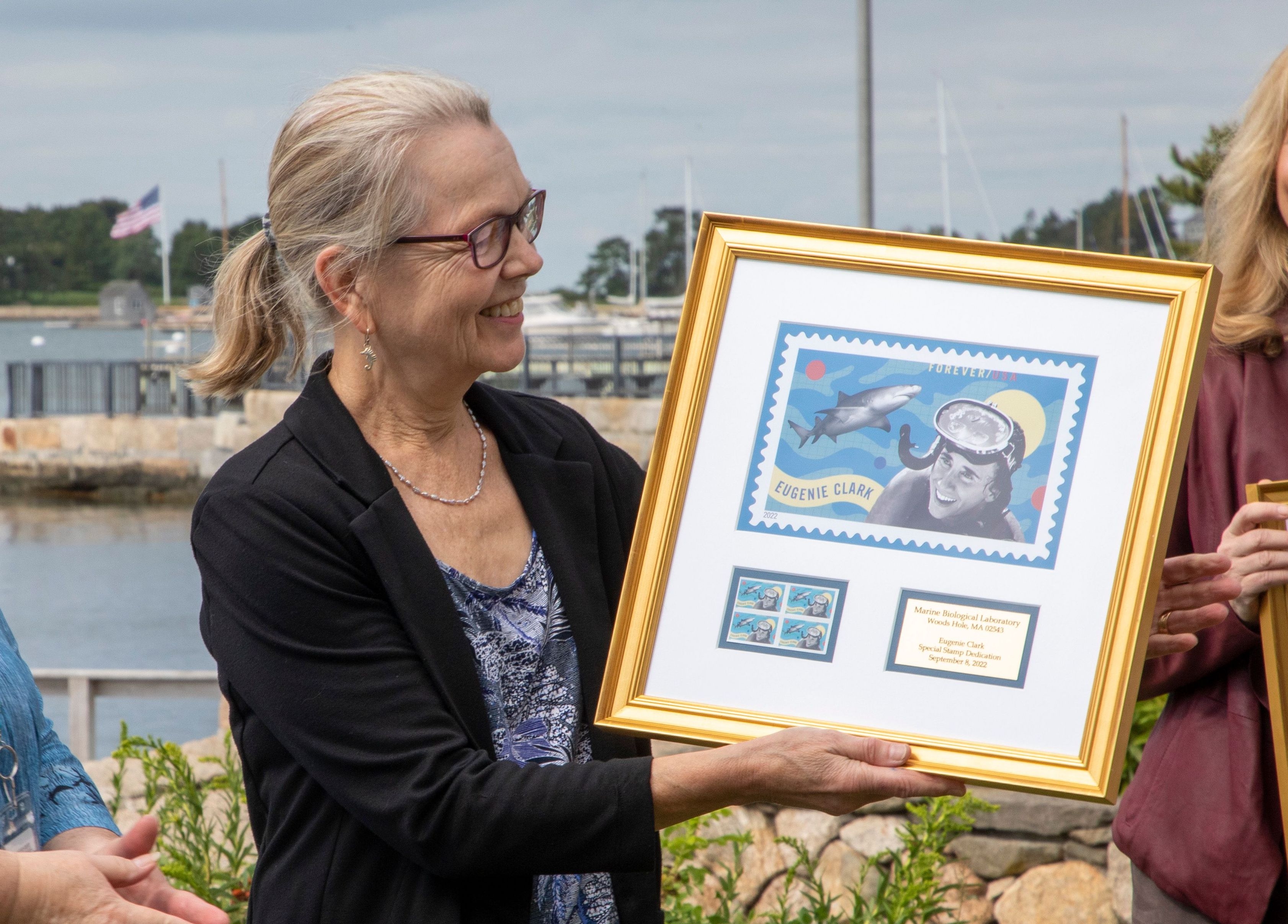 Anne Sylvester, MBL Director of Research, holds a framed print of the Eugenie Clark forever stamp, presented to her by the USPS. Credit: © Woods Hole Oceanographic Institution