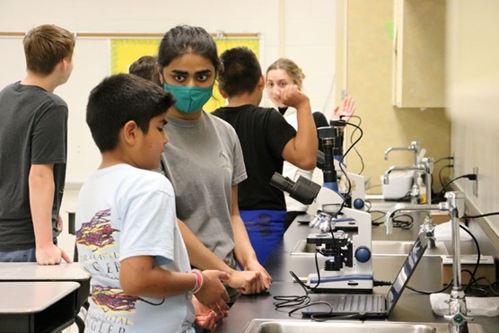 Outreach volunteers help students use the camera-enabled microscopes for the “search and find” activity.
