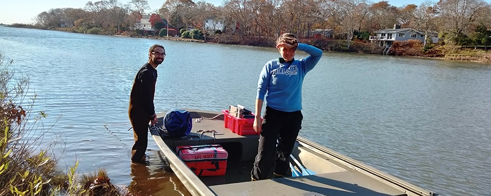 Two people on a boat pulling samples out of the ocean.