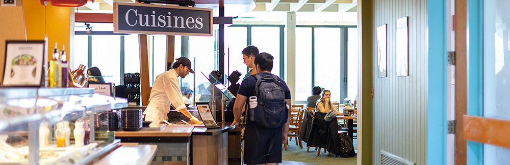 People in Swope Cafe with a "Cuisines" sign hung above a serving station.