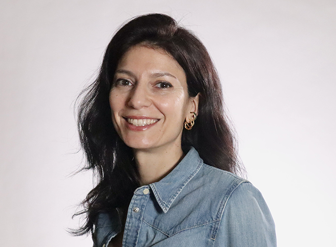 Smiling woman with long dark hair and earrings, wearing a denim shirt.