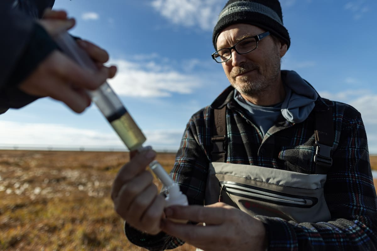 This photo shows a male scientist collecting water samples in a field.