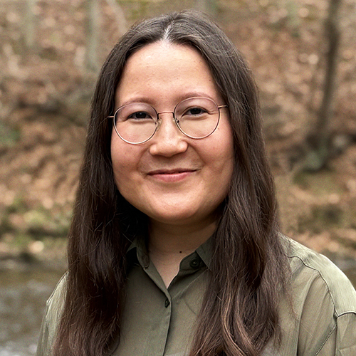 Smiling woman with long dark hair wearing glasses and a dark green shirt.