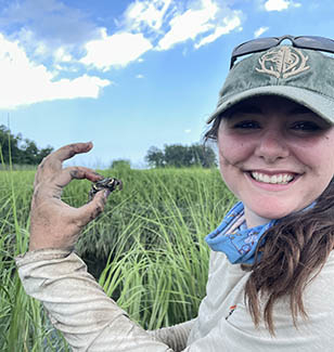 A young woman in a green hat holds up a crab.