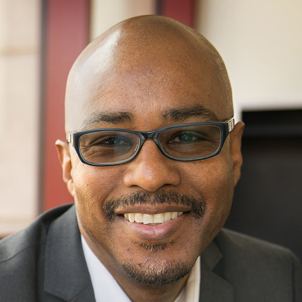 Smiling black man wearing a suit and dark glasses.