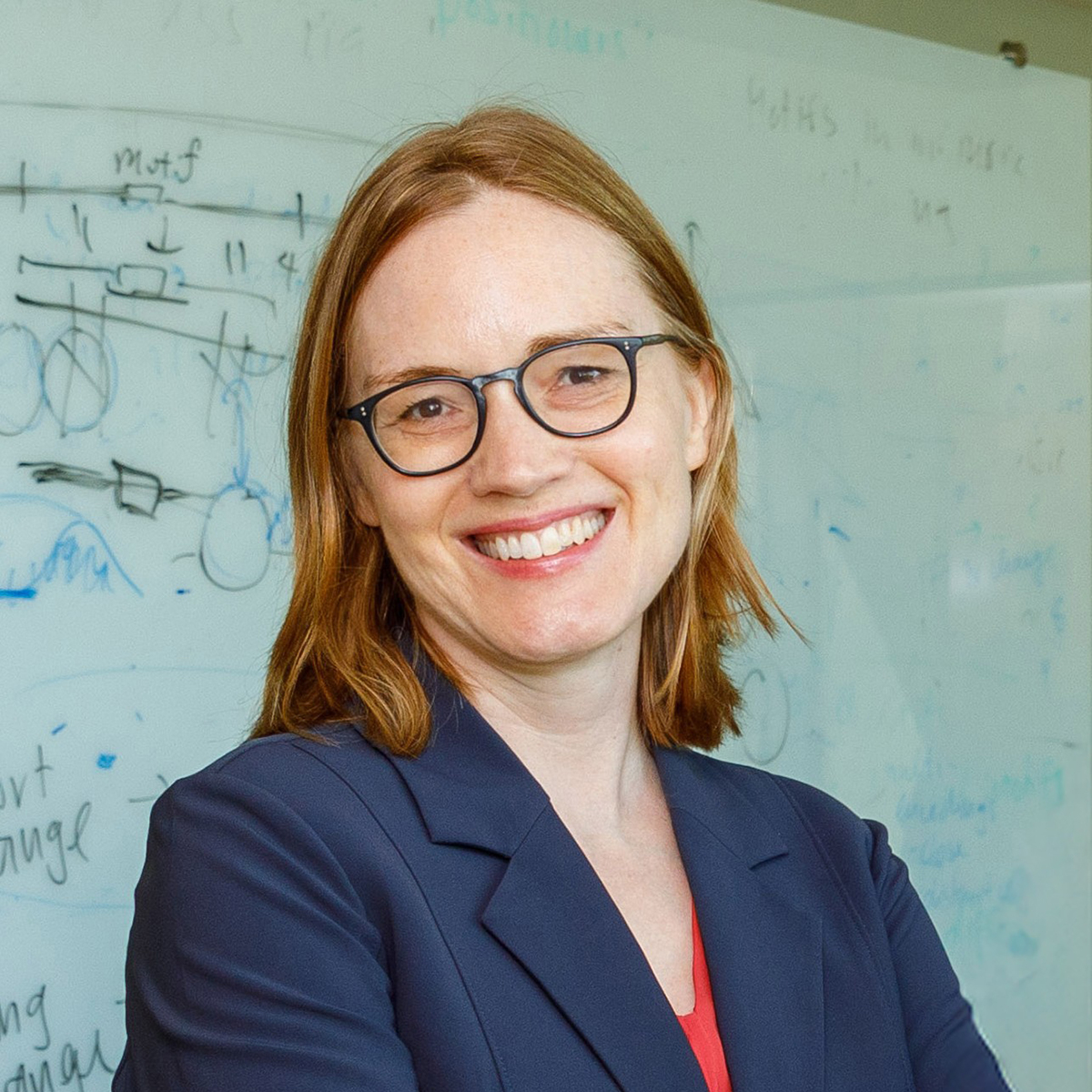 Smiling white woman with brown hair wearing glasses and navy jacket.