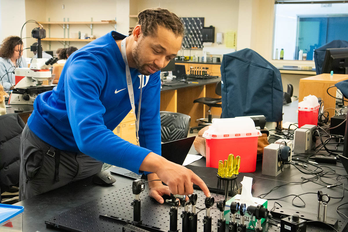 A scientist in a blue shirt examines a micrscope on rails.