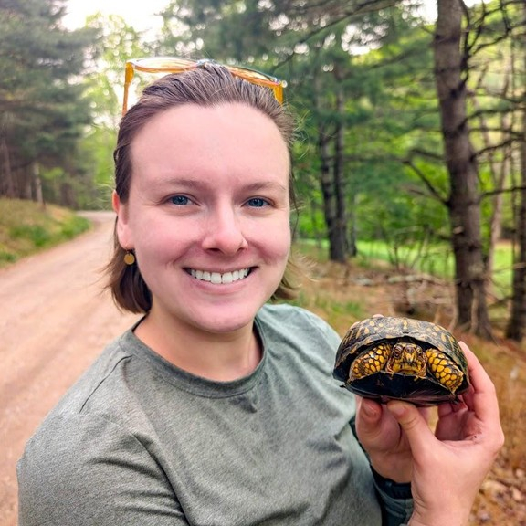 Female presenting person holding a turtle.