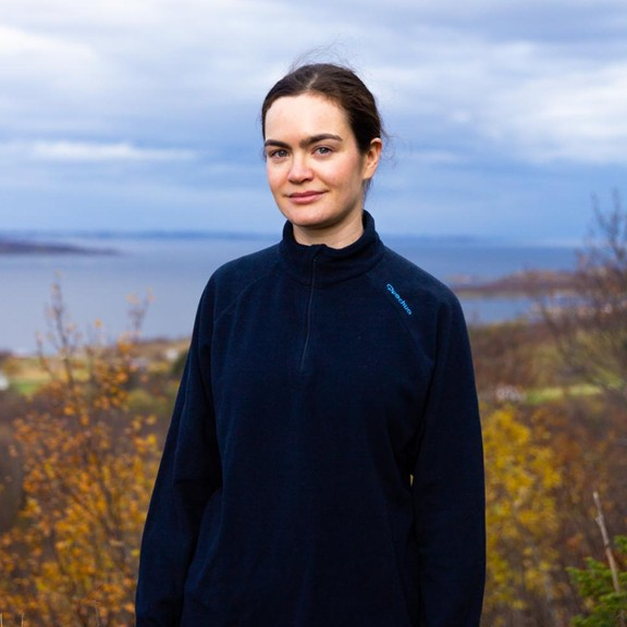 Female presenting person standing in front of a body of water.