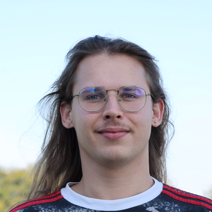 Male presenting person with long brown hair, wearing glasses.