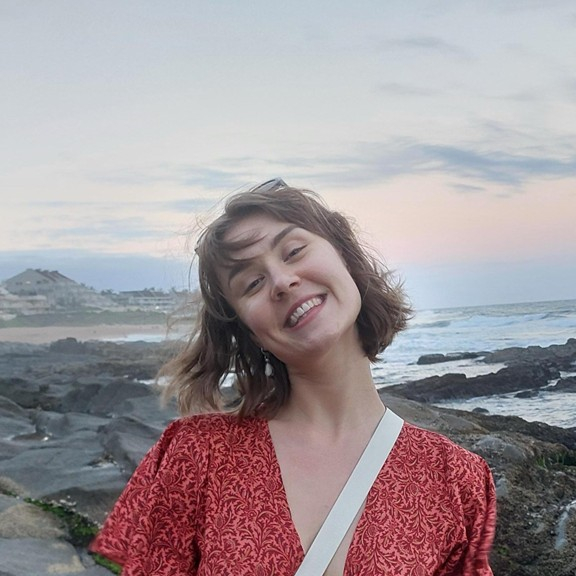 Female presenting person in red dress at the ocean.