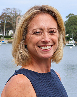 Female presenting person with short blond hair standing in front of the water.