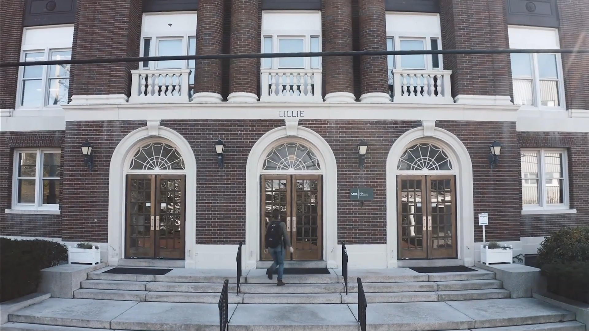 A person walks into Lillie Auditorium, a large brick building on MBL's campus.