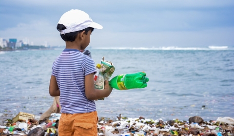 stock image: boy looks out at the ocean, plastic pollution covers the beach