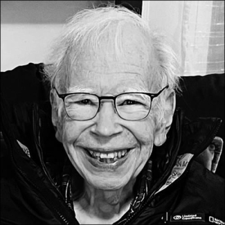 Black and white photo of older smiling man with white hair wearing glasses.