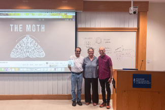 Three people gather by a screen with a logo of a moth on it.