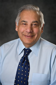 Male presenting person with short gray hair wearing a blue shirt and tie.