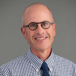 Male presenting person wearing glasses and checked shirt with tie.