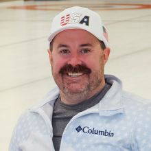 Male presenting person with Team USA hat, on ice.